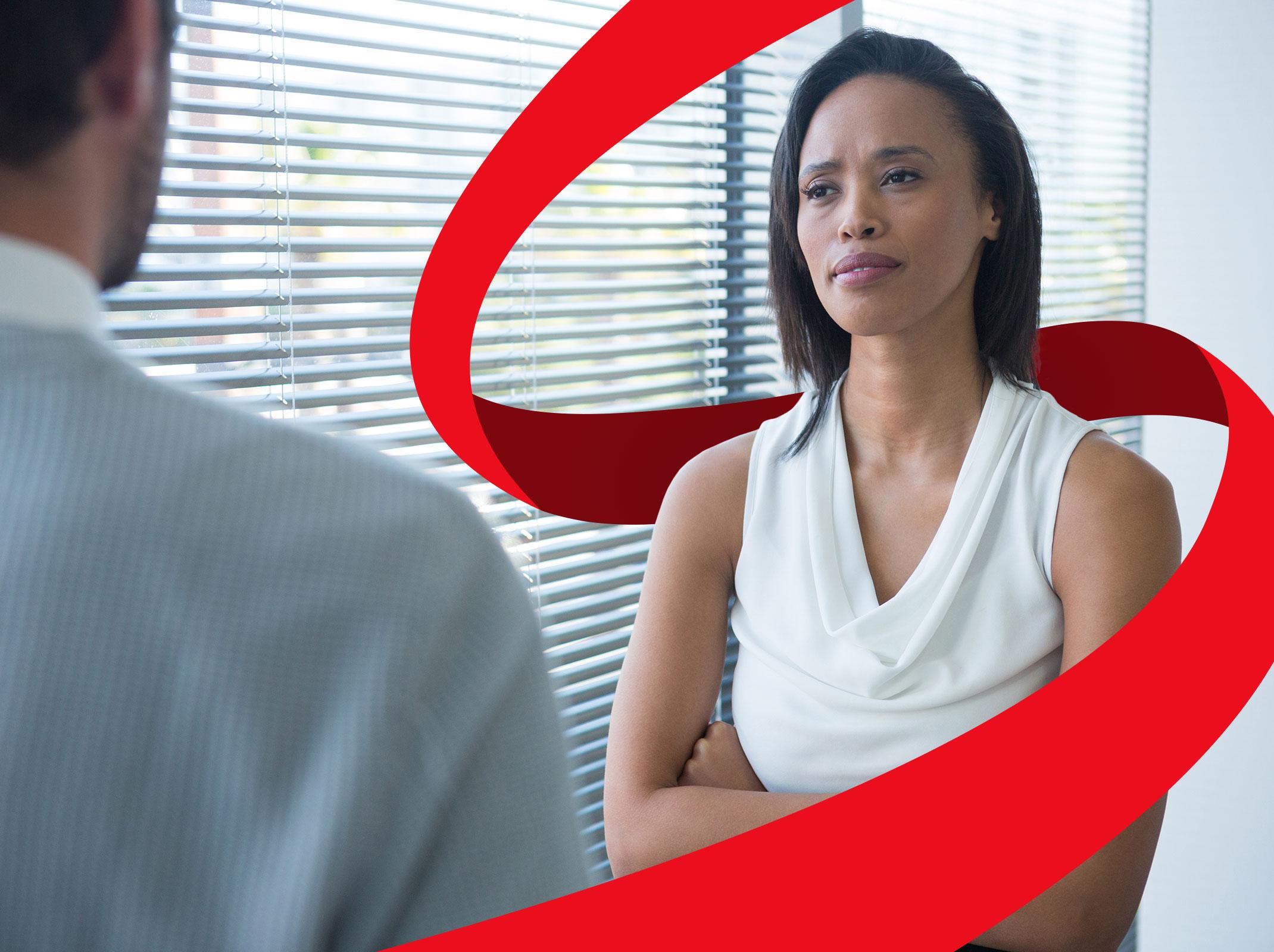 A female business professional looking uncomfortable as she has a conversation with another business professional.  They are in an office setting.