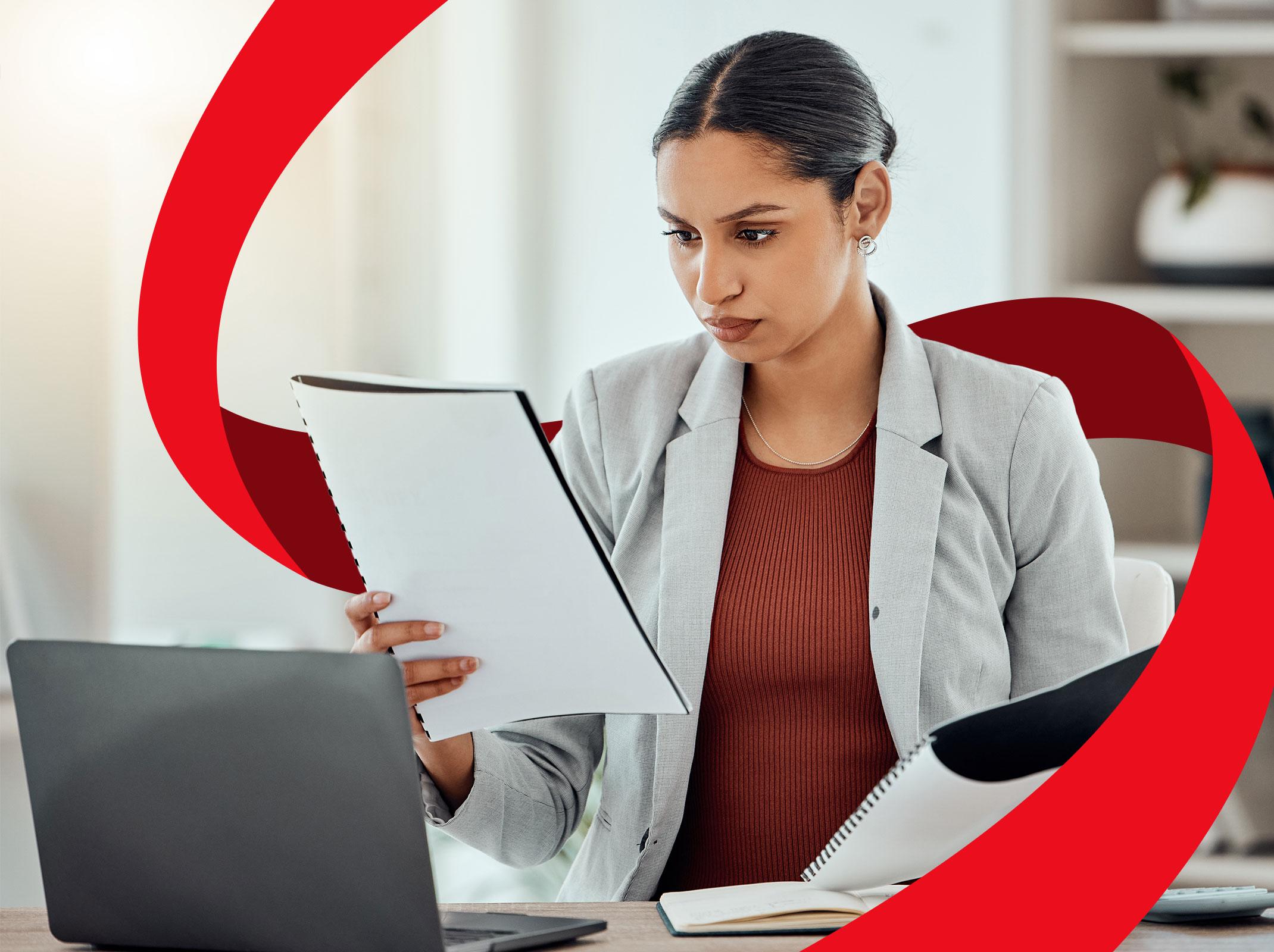 A Human Resources professional reviewing documents in front of a laptop in an office setting.