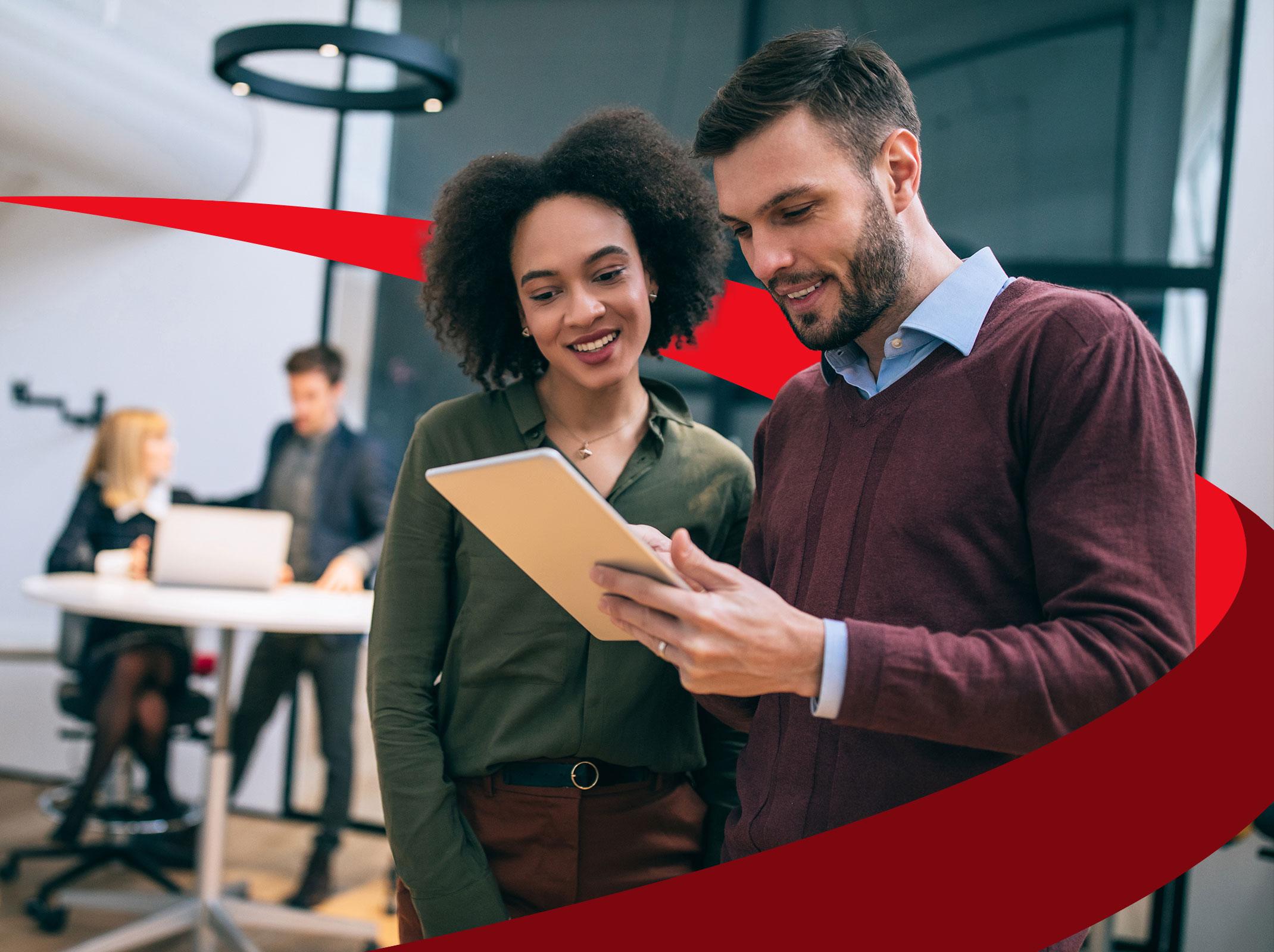 A leader in a business setting providing feedback to another business professional.  They are reviewing something on a tablet and smiling.