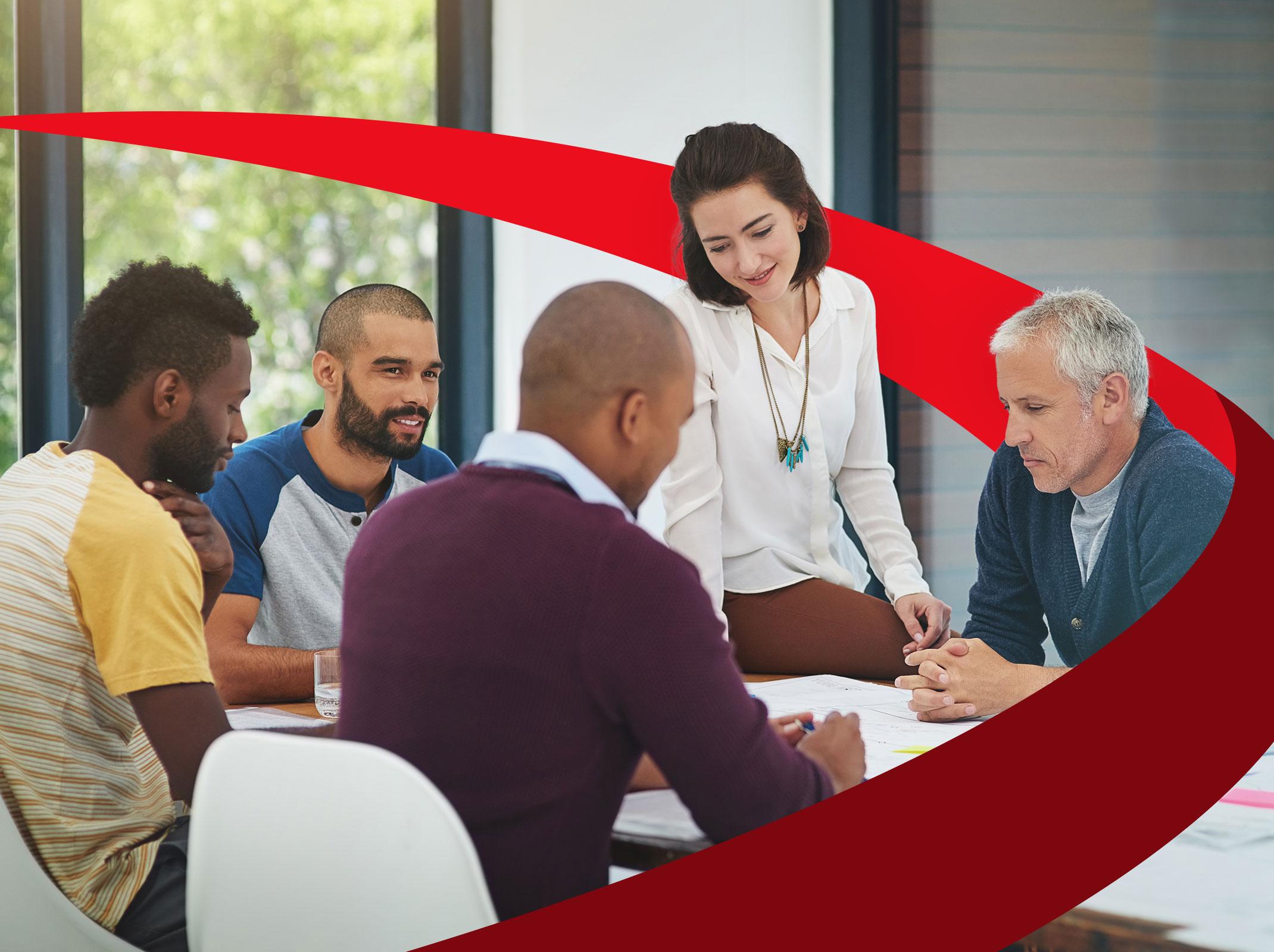 A group of professionals working around a table.  They are smiling and reviewing documents.  One appears to be the leader of the group. 