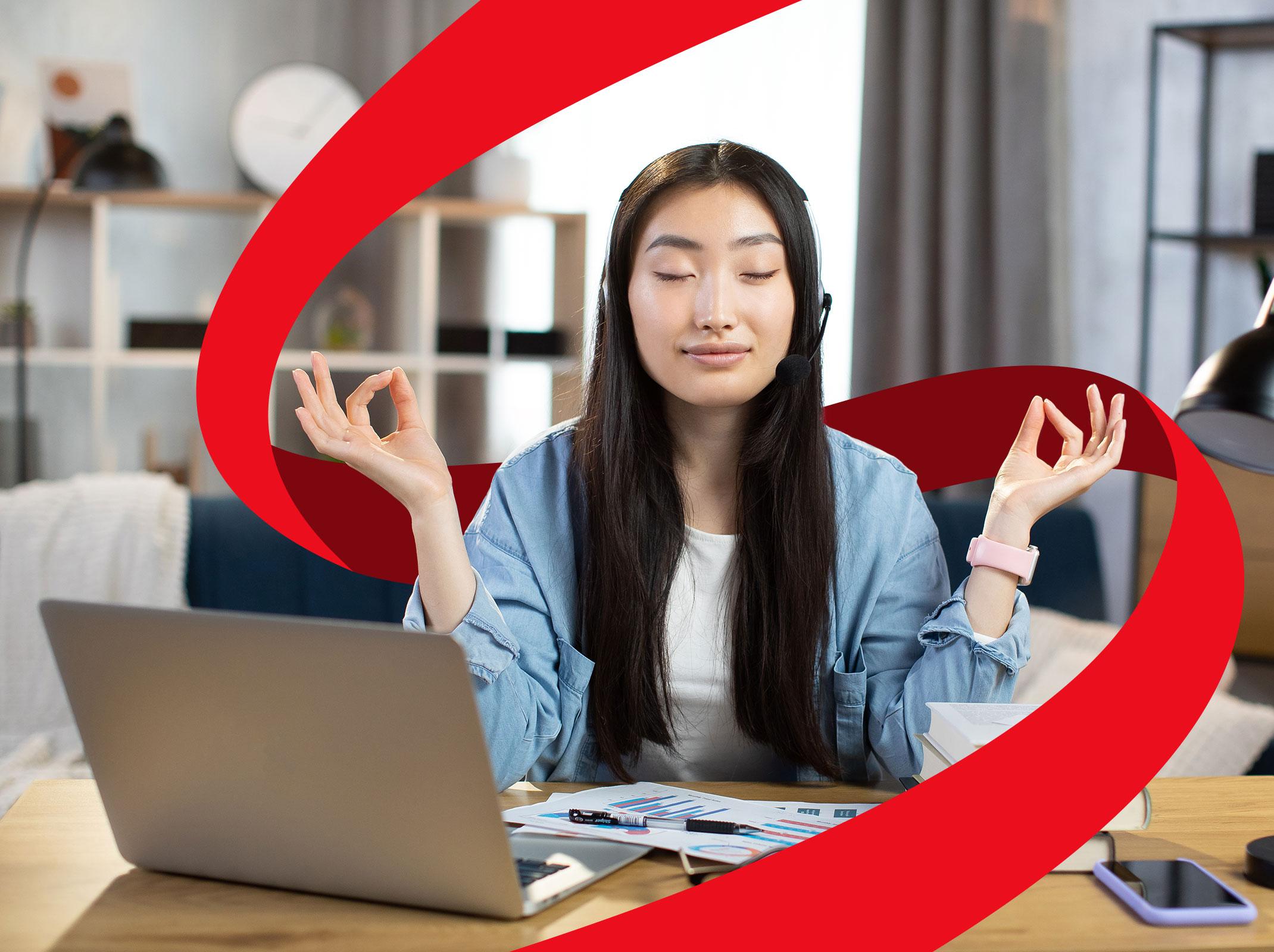Female working at a laptop. She has her eyes closed and appears to be meditating.