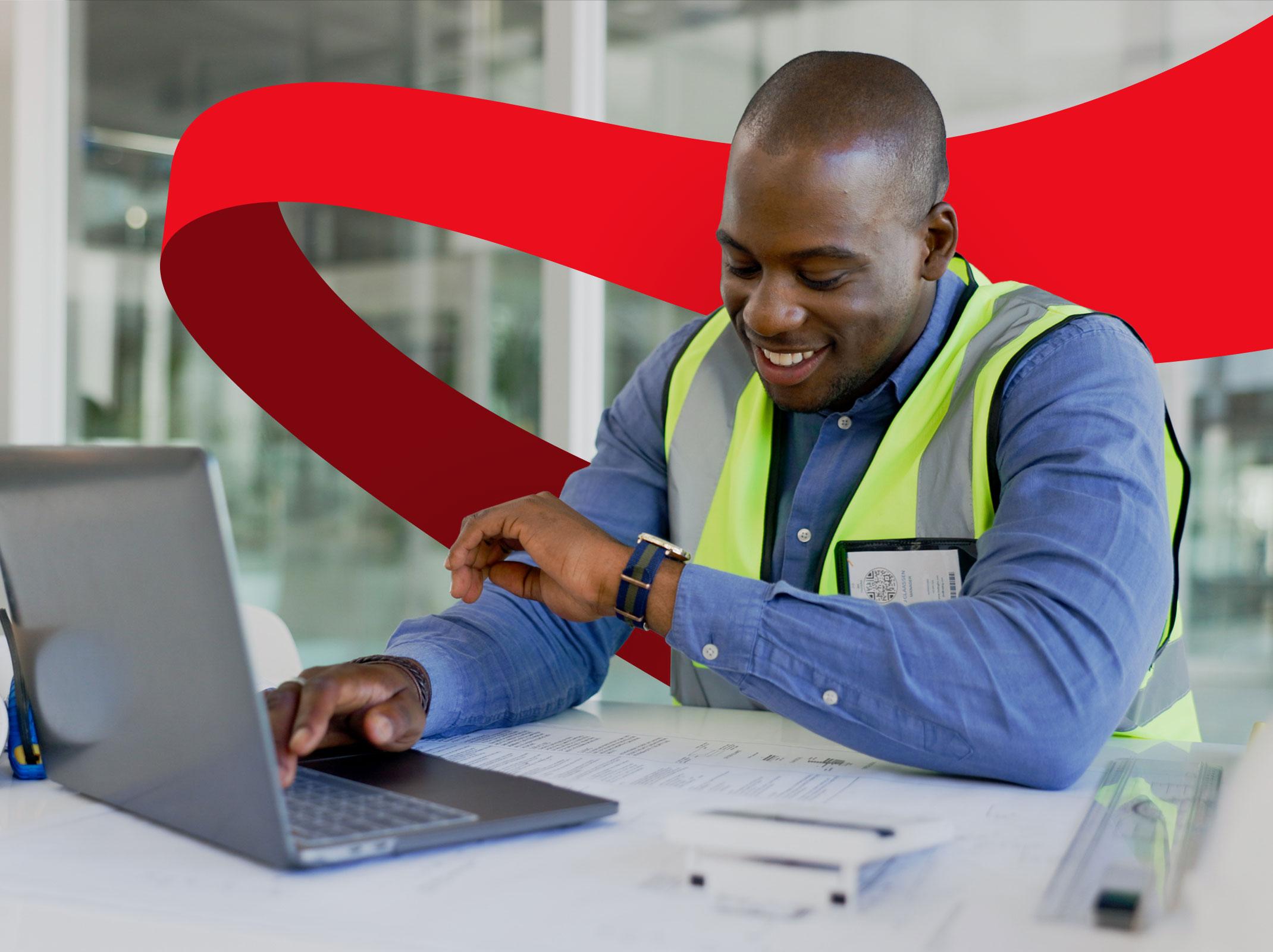 Manufacturing professional working on a laptop with some paperwork in front of him.