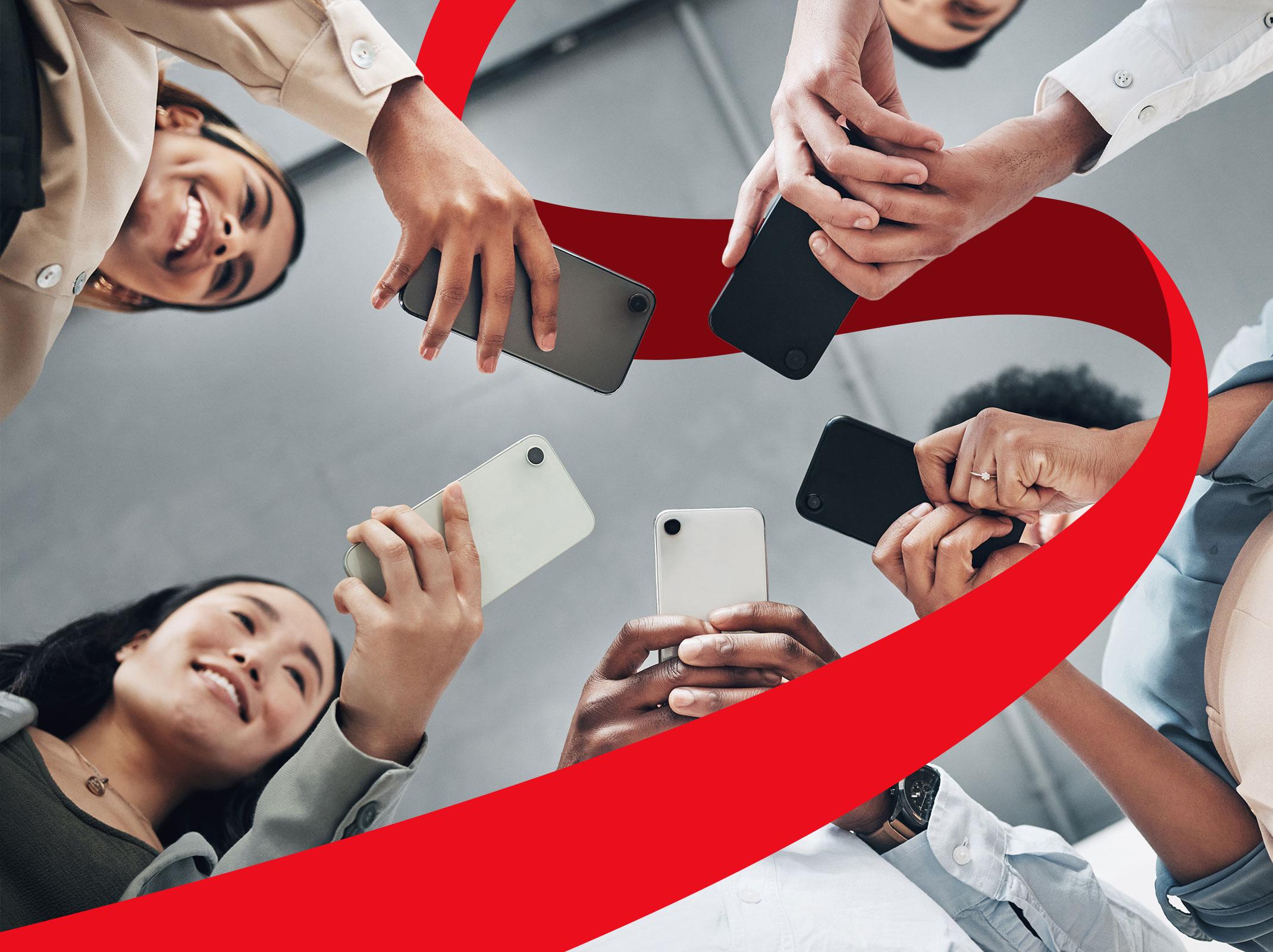 A group of business professionals using their phones to view social media. The image is looing up on the smiling business professionals.