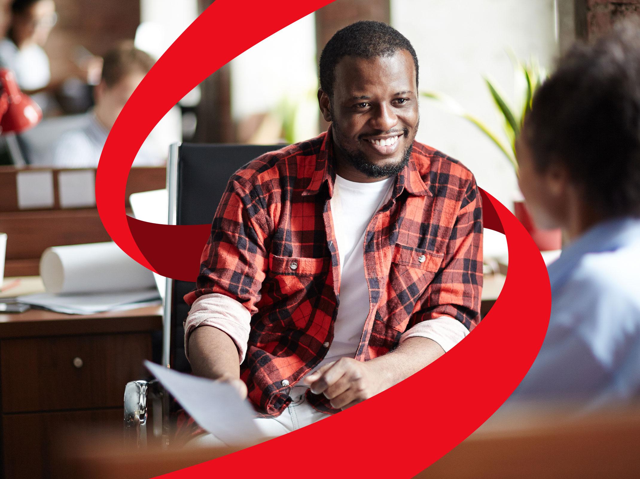 A leader giving performance feedback to an employee in an office setting.  They are sitting at a desk with papers between them.