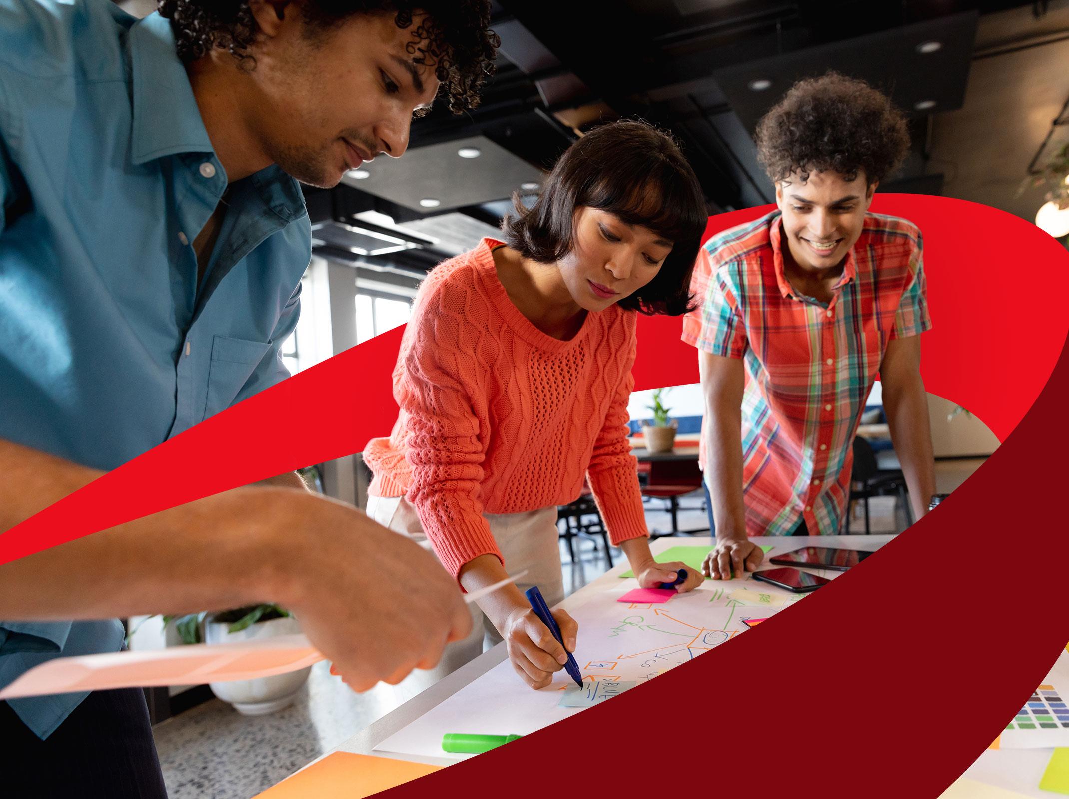 Three creative business professionals working on something on a conference table.  They are standing in a business setting and appear to be collaborating.