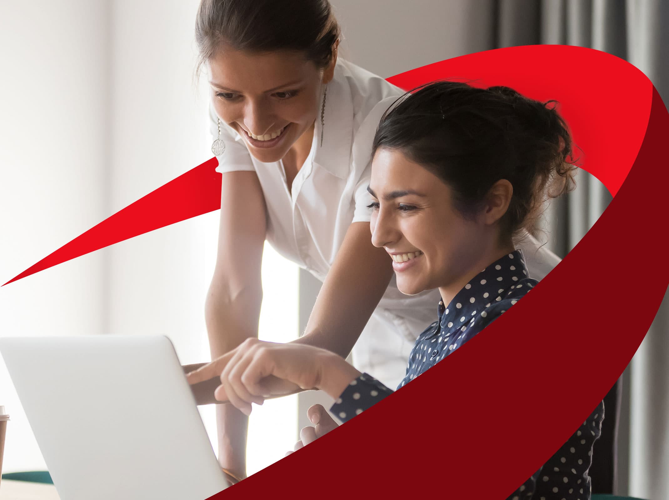 Two female business leaders reviewing something on a laptop. One is pointing at the screen and both are smiling.